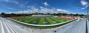 Panoramic view of a football field from the stands, showing yard lines and end zones under a partly cloudy sky.