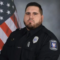 Portrait of a Racine Police officer in uniform, with the American flag blurred in the background.