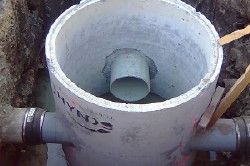 Concrete manhole with pipe connections in a trench, viewed from above. Construction or repair site.