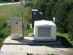 Electrical control boxes and equipment on a concrete pad in a grassy area.