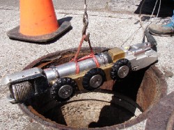 Sewer inspection robot being lowered into manhole for underground pipe assessment and maintenance.