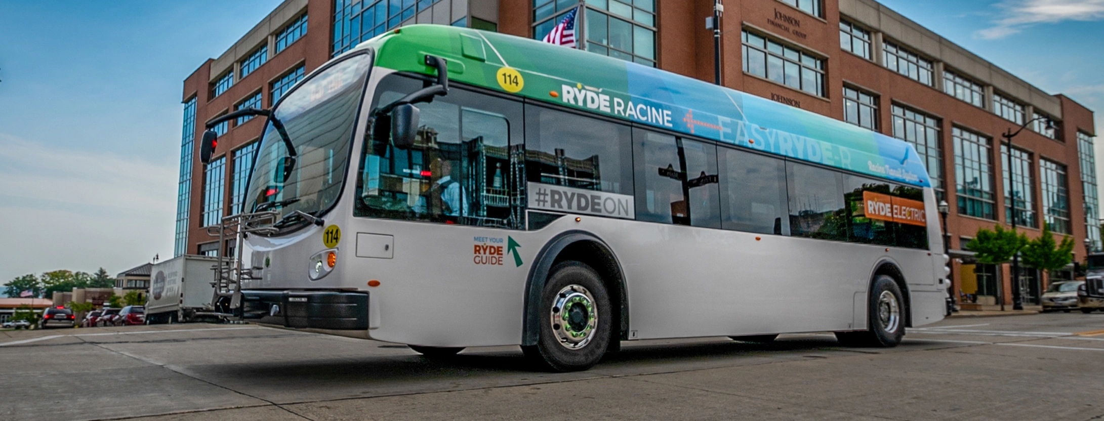 Ryde Racing bus parked in front of a brick building, door open, on a sunny day.