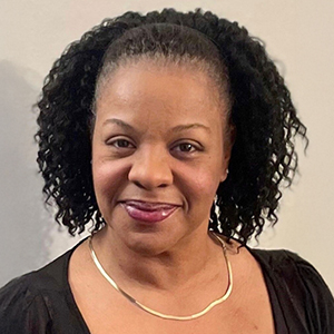 Headshot of a smiling Black woman with curly hair, wearing a gold necklace and a black top.