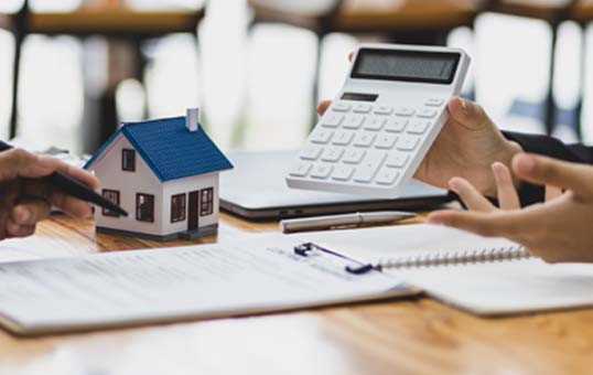 Home purchase discussion with calculator, contract, and model house on a table.
