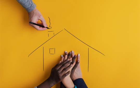Hands of diverse people supporting a drawn house on a yellow background, symbolizing community support for housing.
