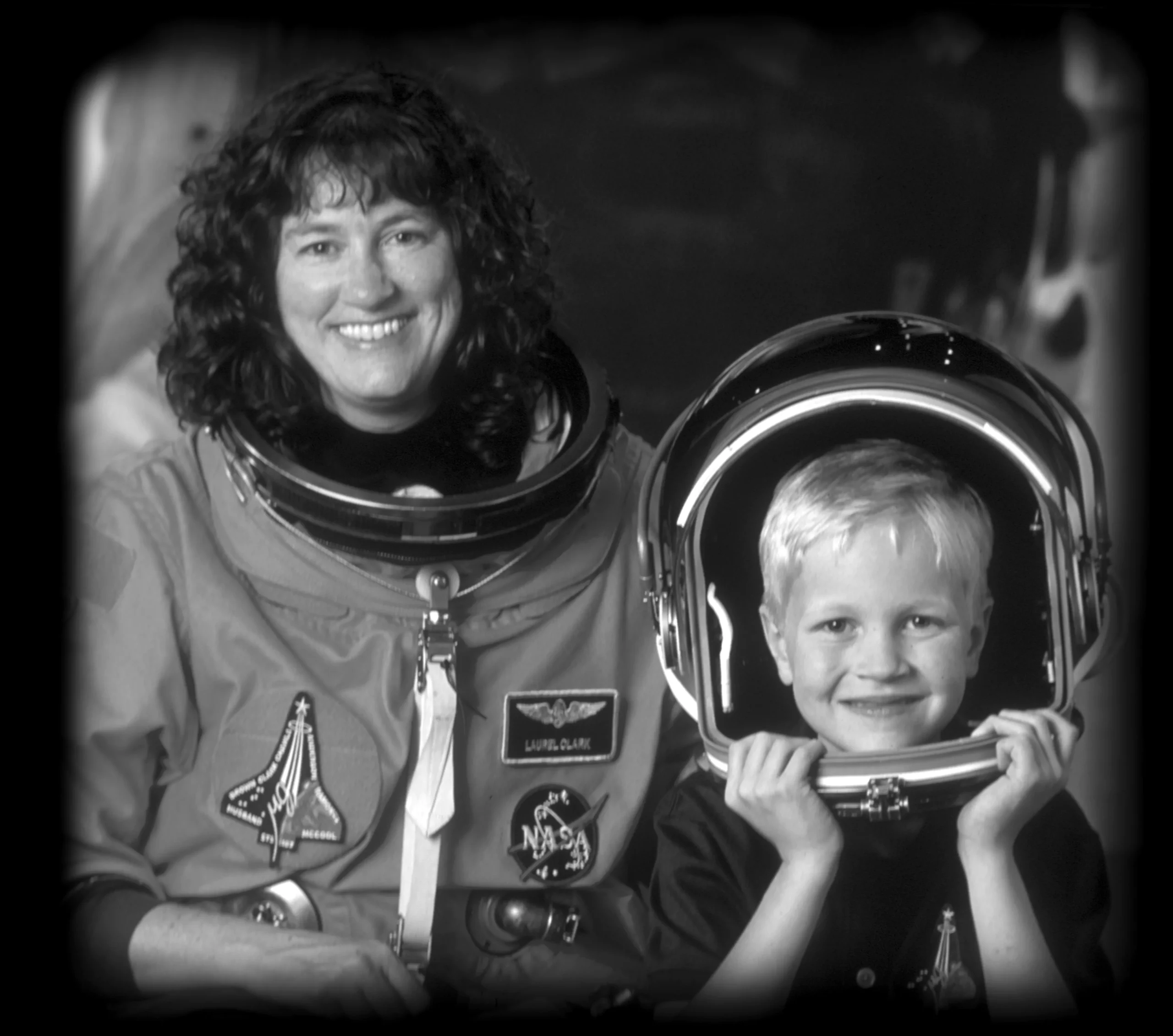 Astronaut Janice Voss with a child wearing a space helmet, both smiling in a black and white portrait.
