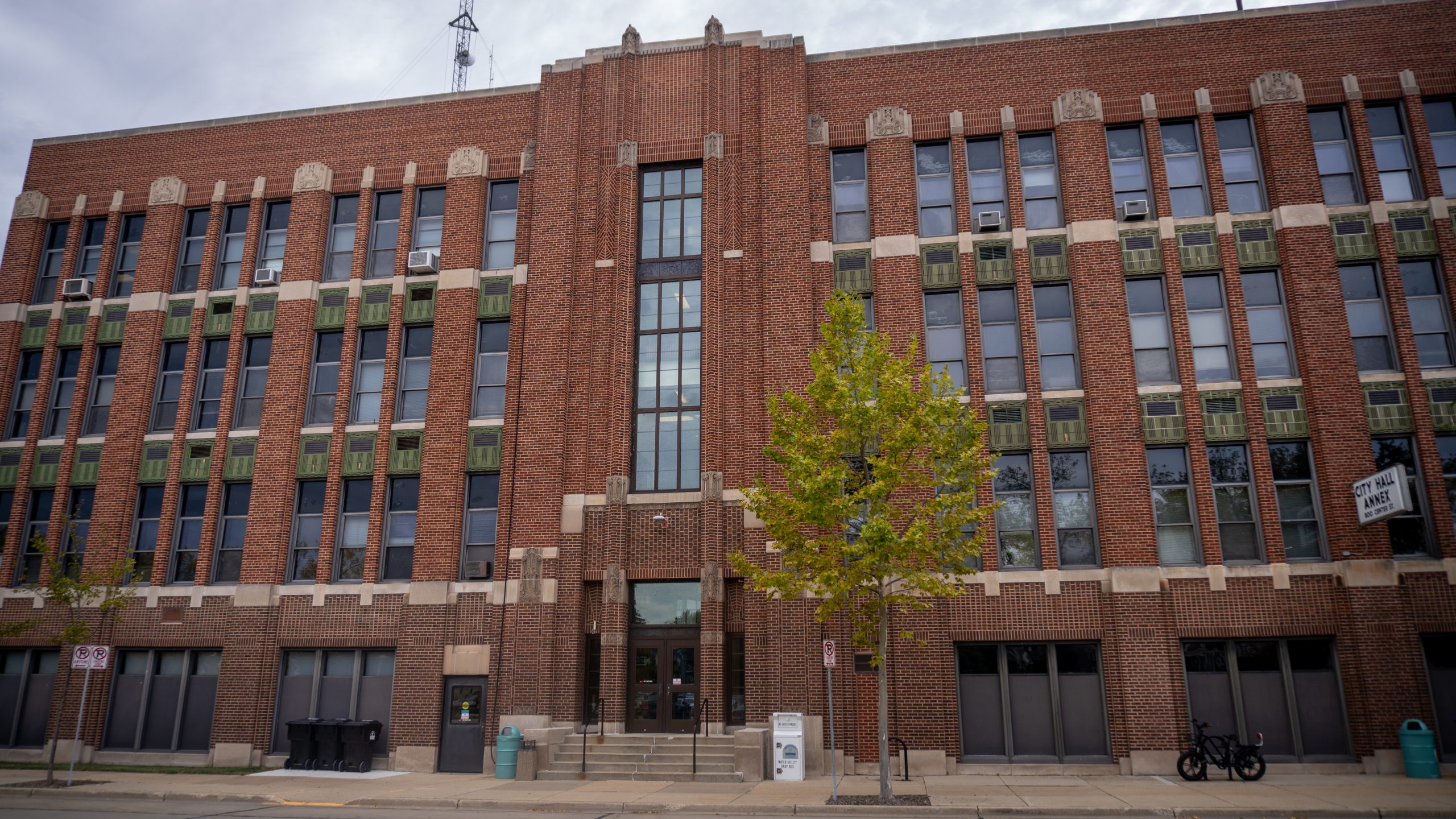 Exterior of a three-story brick building with art deco details and a tree in front. Cloudy sky in the background.