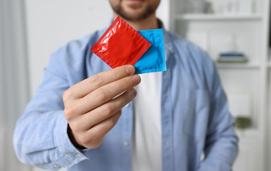 Person holding a red and a blue condom packet in their hand, promoting safe sex and contraception.