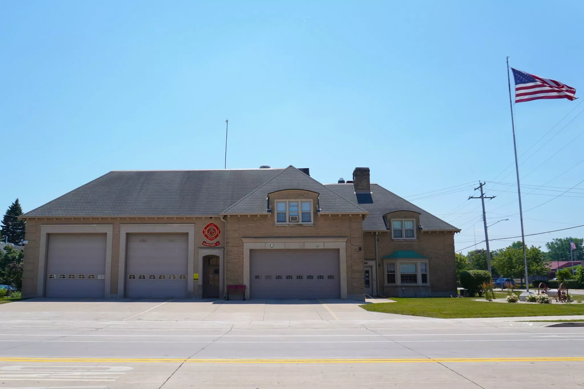 Exterior of a fire station with three garage doors and an American flag waving in the background.