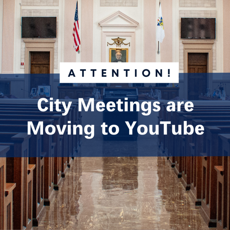 City meetings moving to YouTube. Interior view of a meeting hall with American and city flags.