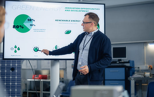 Male Engineer Points at Big Screen With Presentation and Talks About Green Energy and Solar Panels Future Possibilities. Engineering and Sustainable Energy Education Concept.