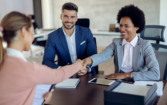 Woman shaking hands with interviewer. Two interviewers at desk, one smiling. Job interview or business meeting.