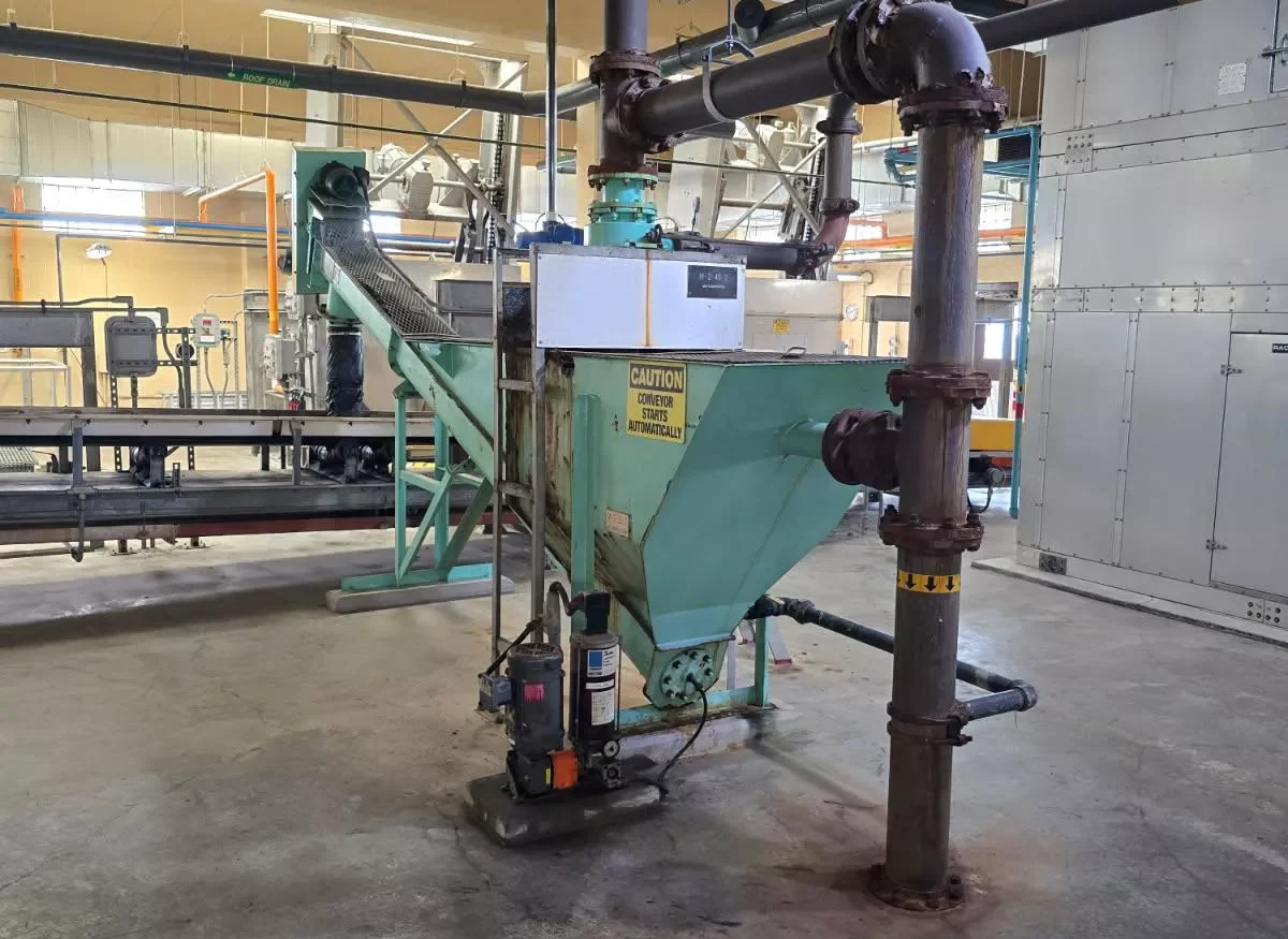 Industrial machinery with pipes and conveyor belt in a factory setting. Focus on equipment details.