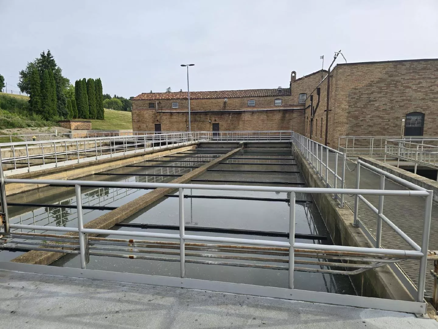 Water treatment plant settling tanks with metal railings and brick building in the background.