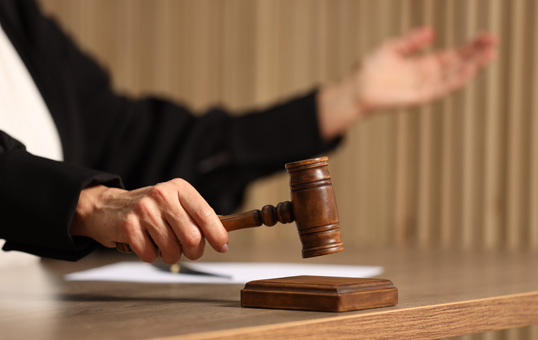 Judge holding gavel in courtroom, gesturing with open hand. Represents legal proceedings or judicial decisions.