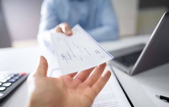 Close-up of a hand receiving a paycheck from another person in an office setting.