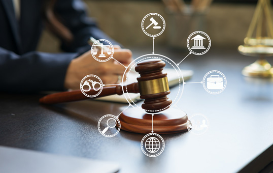 Gavel on desk with legal icons representing law, justice, and legal services. Person writing in background.