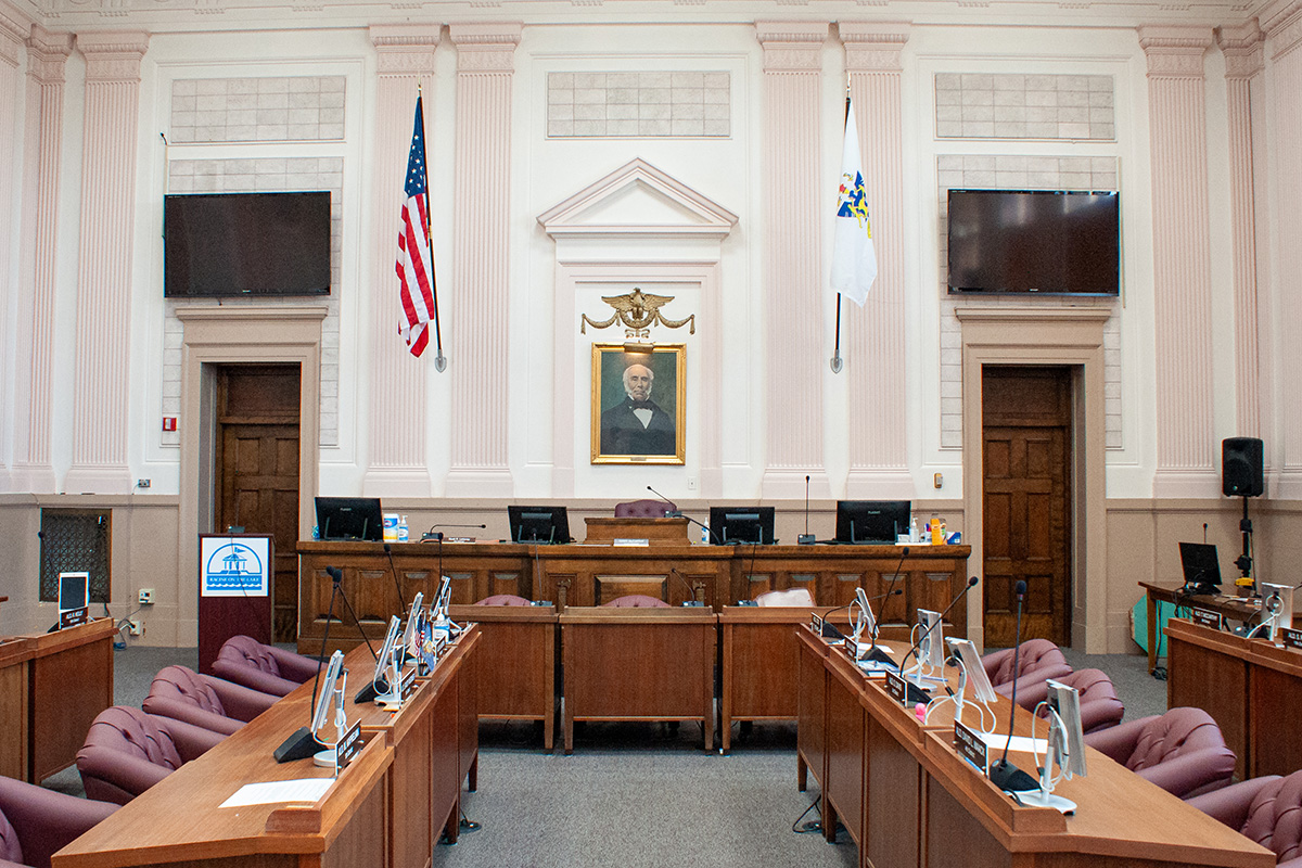 Interior of a government chamber with flags, monitors, and seating for officials and the public.