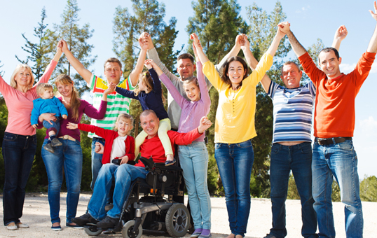 Group of diverse people with disabilities and allies raising their hands in celebration outdoors.