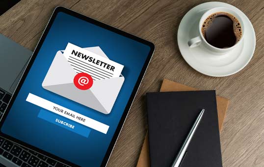 Newsletter subscription form on a tablet screen with a laptop, coffee, and notebook on a wooden desk.