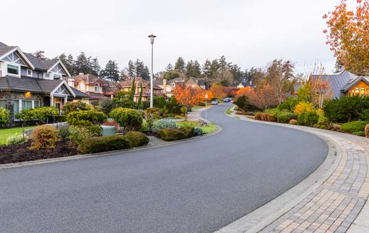 Curving street in a suburban neighborhood with well-maintained houses and landscaping, taken during autumn.