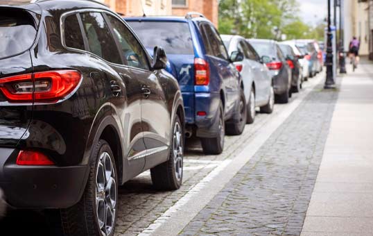 Cars parked in a row along a cobblestone street, showcasing various vehicle models and colors.