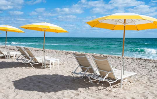 Beach scene with yellow umbrellas and lounge chairs on the sand, ocean and blue sky in the background.