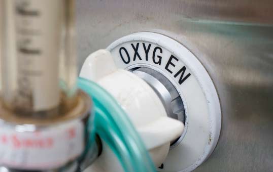 Close-up of an oxygen flow regulator with a white knob and the word "OXYGEN" printed on it.