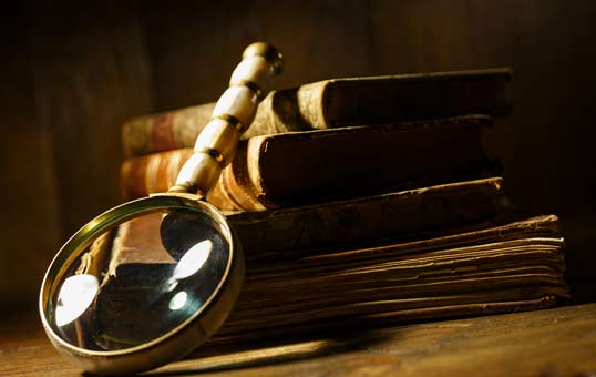 Magnifying glass resting on a stack of old, leather-bound books. Focus on research, history, or investigation.