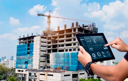 Construction site monitored on a tablet with charts and data, crane and building in background.