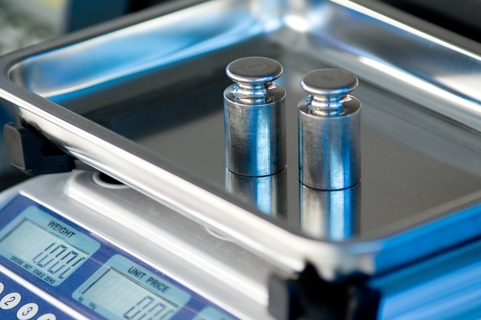 Two metal weights on a digital scale displaying 1.00L, used for precise measurement and calibration.