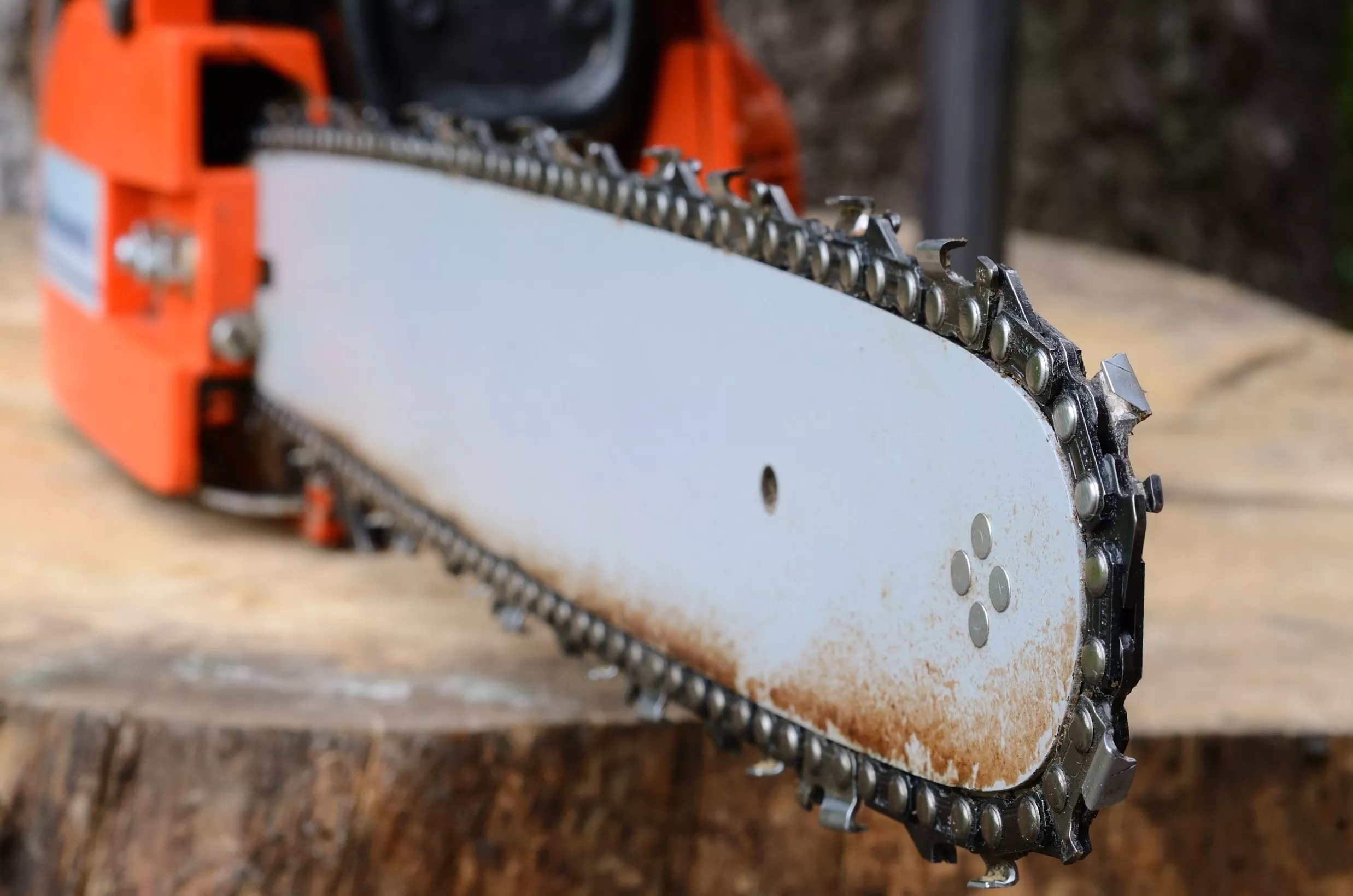 Close-up of a chainsaw blade on a tree stump. The chainsaw is orange and black.