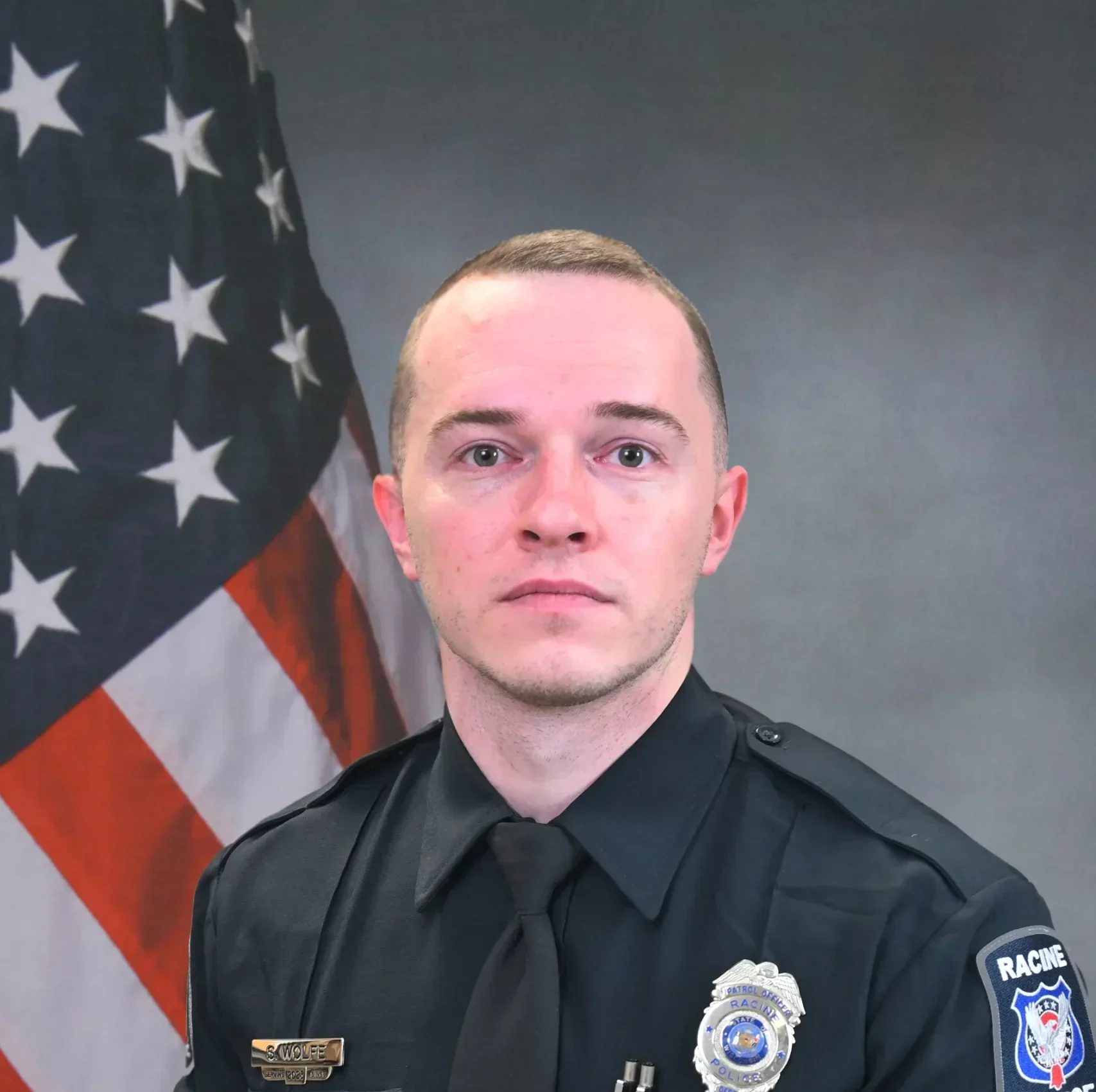 Official portrait of a police officer in uniform, with the American flag in the background.