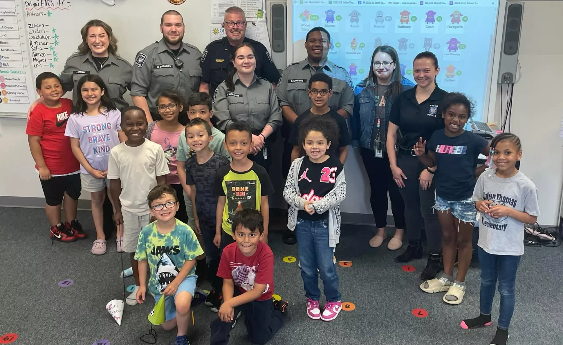 Group photo of elementary students with police officers in a classroom setting.