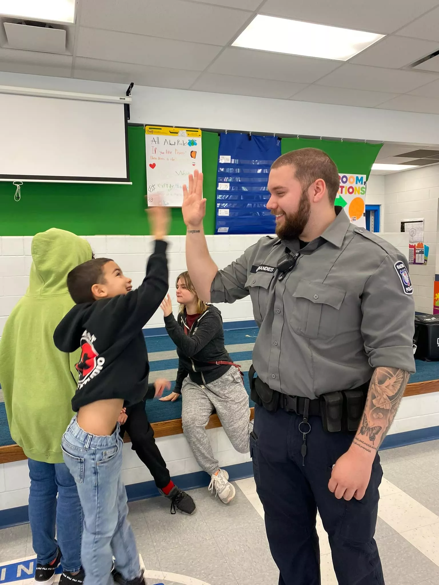 School resource officer gives a student a high five in a school hallway. Other students are nearby.