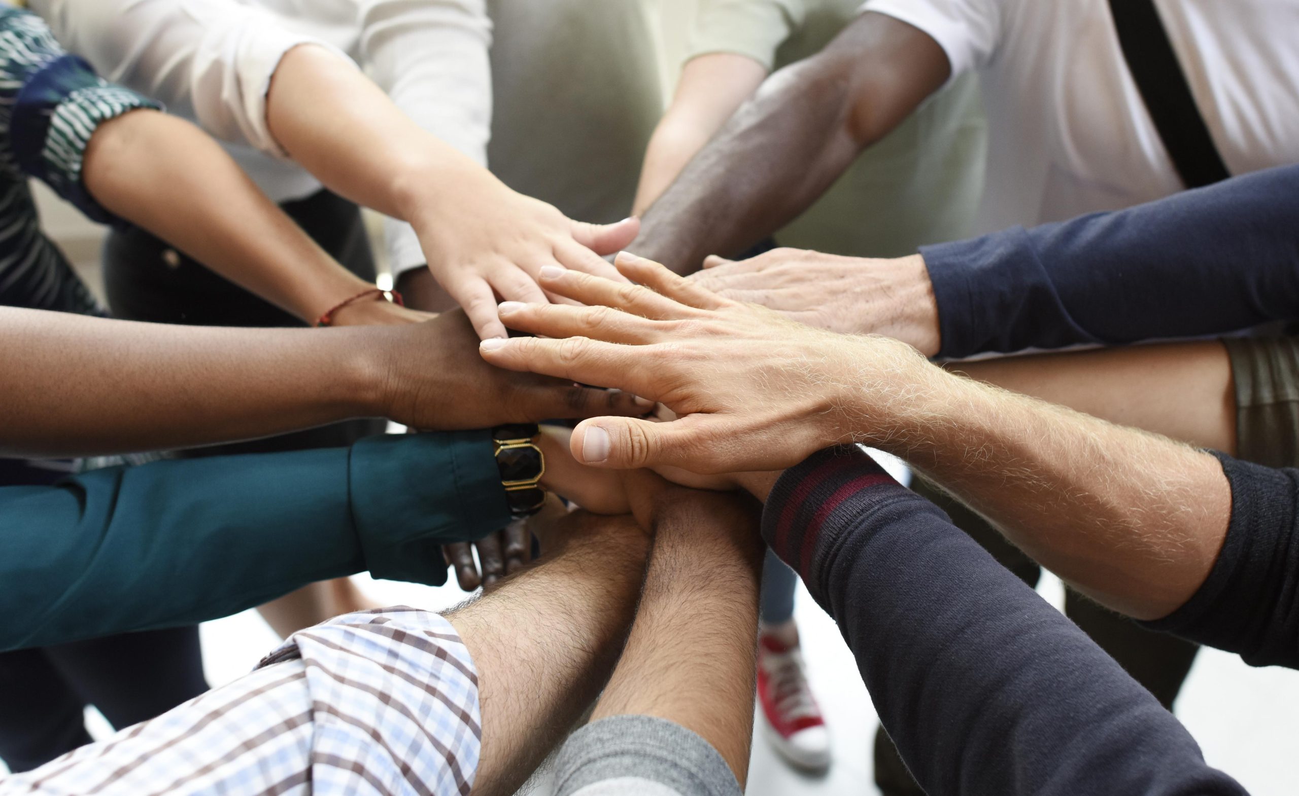 Diverse group of people with hands stacked together in a show of unity and teamwork.