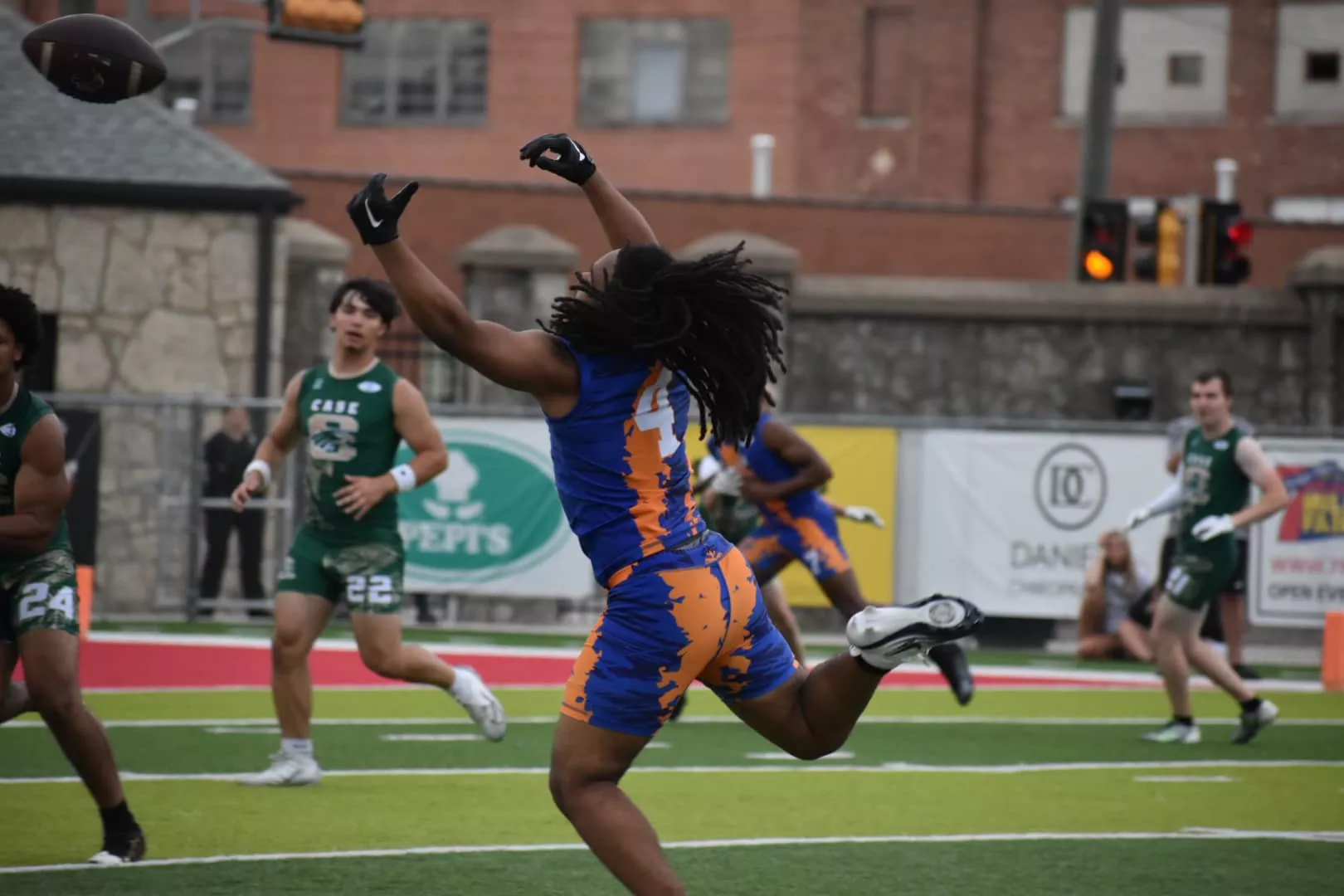 Football player in blue and orange jersey jumps to catch a pass during a game.
