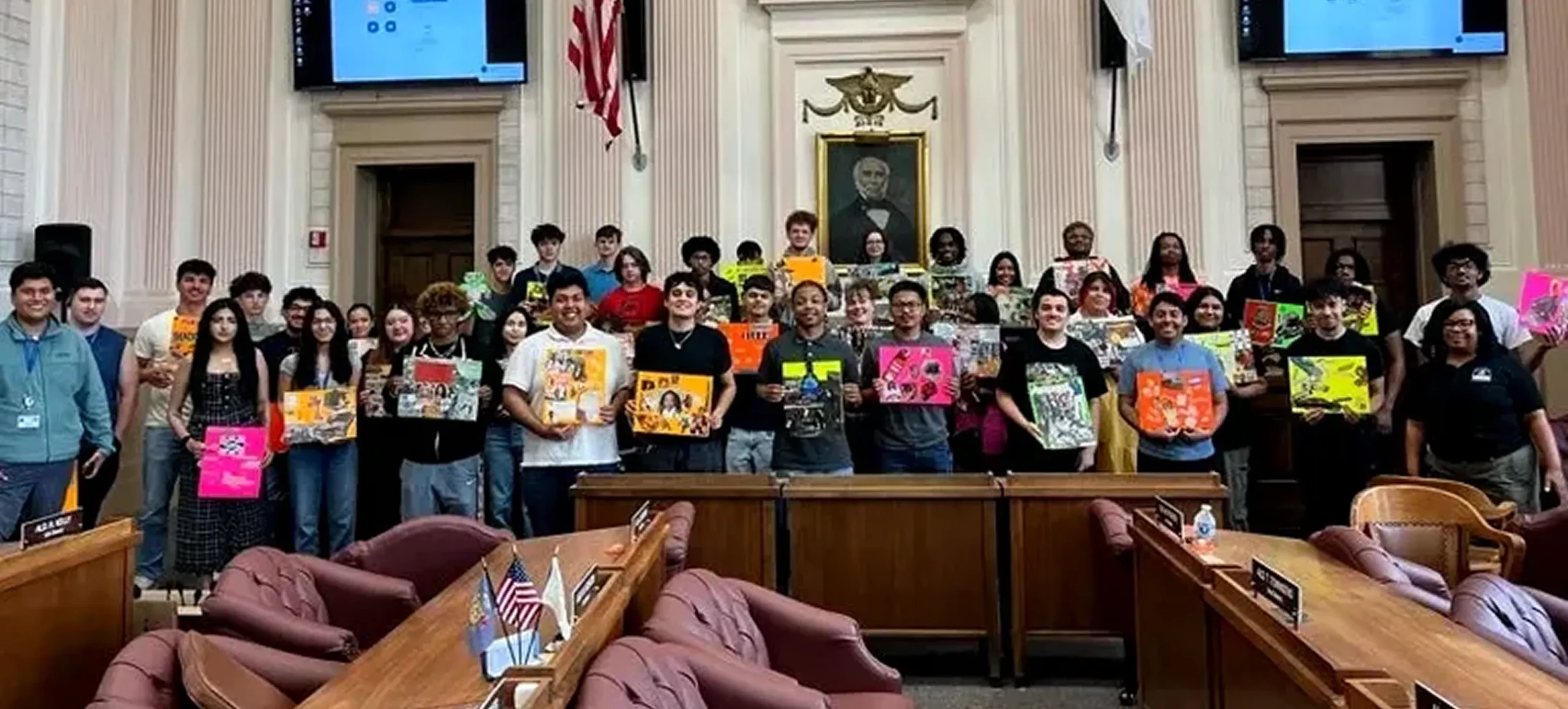 Group of students holding signs in a government building, possibly advocating for a cause or participating in a civic event.