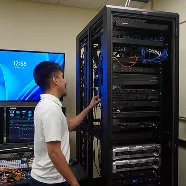 Technician working on a server rack in a data center, with a monitor displaying the time in the background.