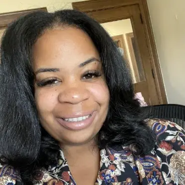 Headshot of a Black woman with shoulder-length black hair, wearing a floral print top, smiling at the camera.
