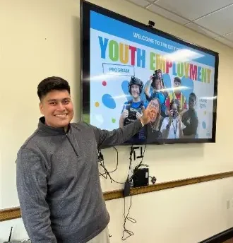 Man presenting Youth Employment Program on a large screen, smiling and pointing at the display.