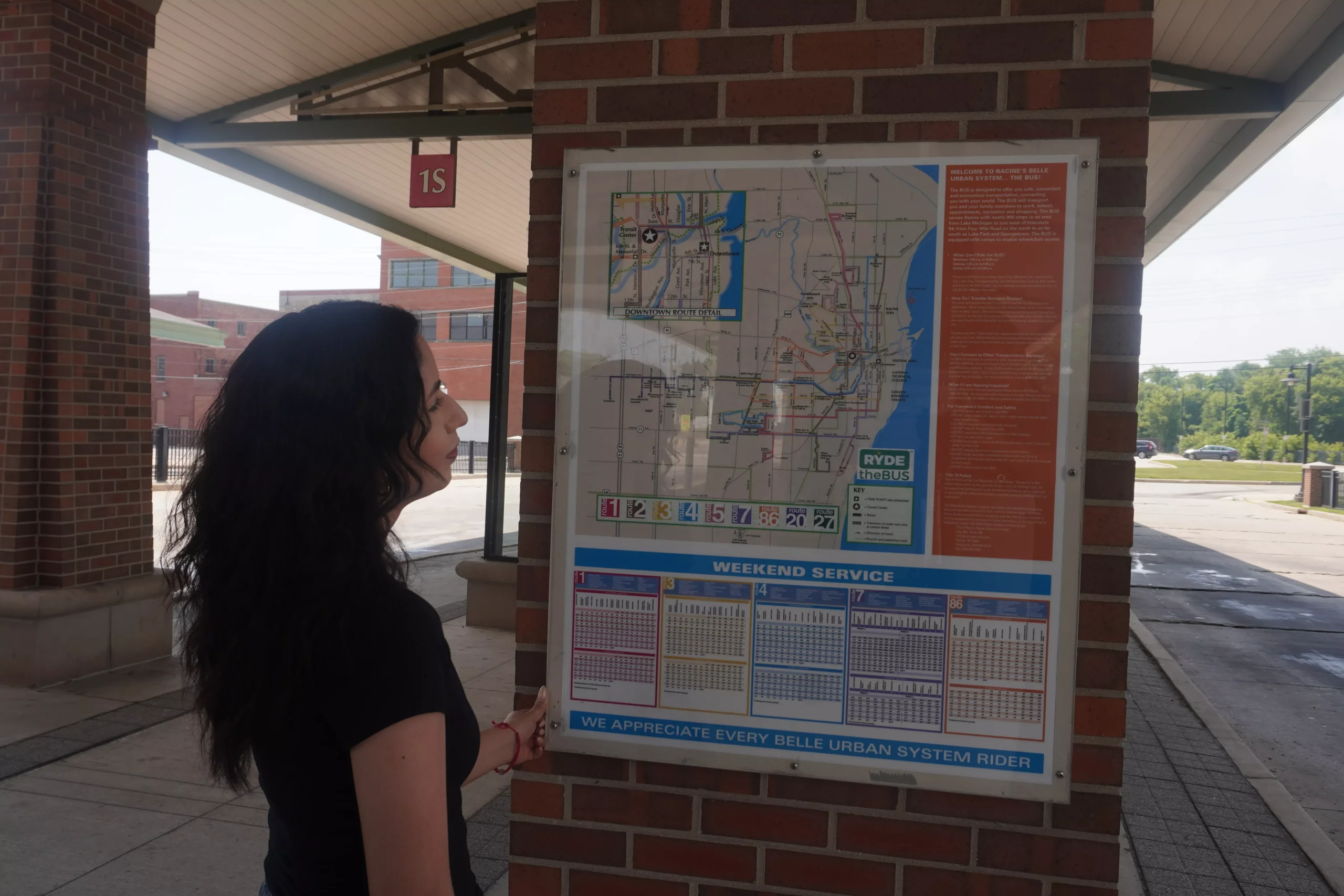Woman at bus stop shelter looking at a map of the bus routes and schedule.