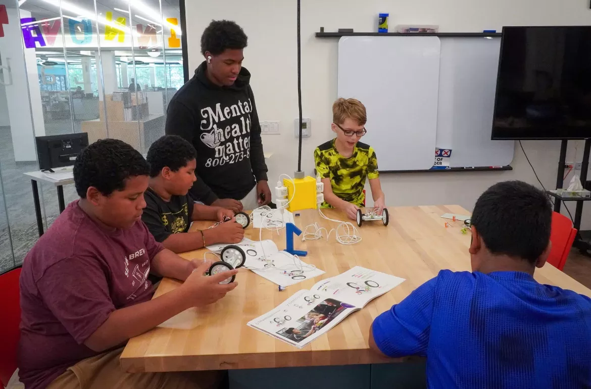 Group of students collaborating on a robotics project around a table with instructions and robot parts.