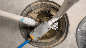 Sump pump system with pipes and float switch in a pit filled with water, installed in a concrete floor.